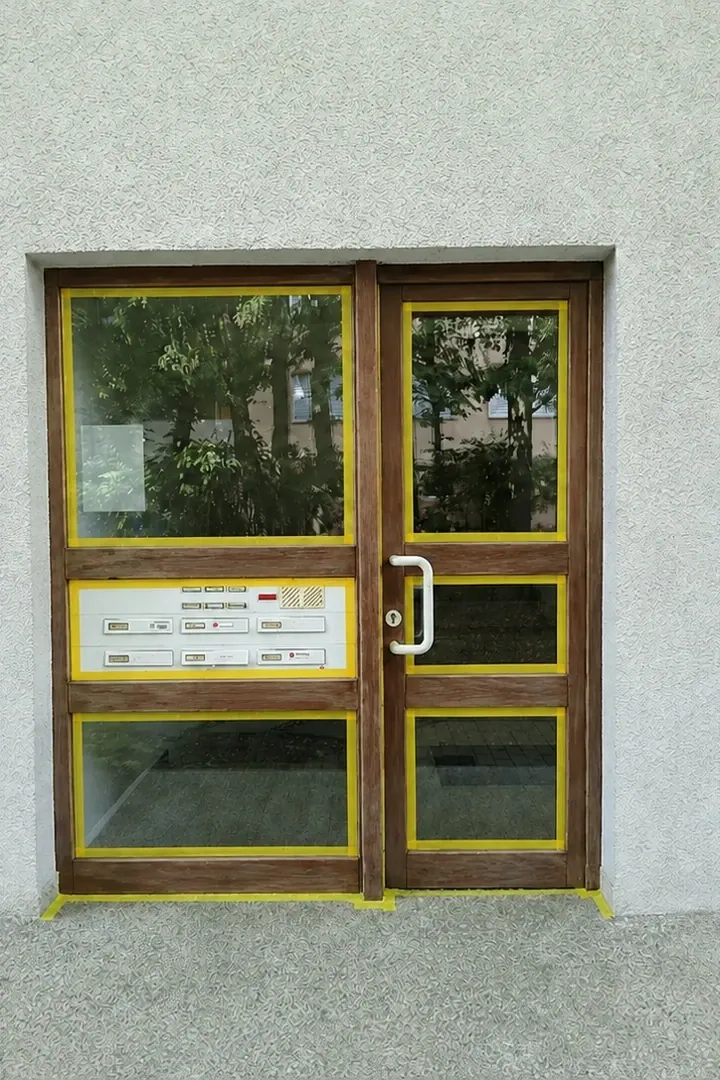 Braune Holzhaustür mit abgeklebten Glasflächen und Klingelfeld vor der Überarbeitung